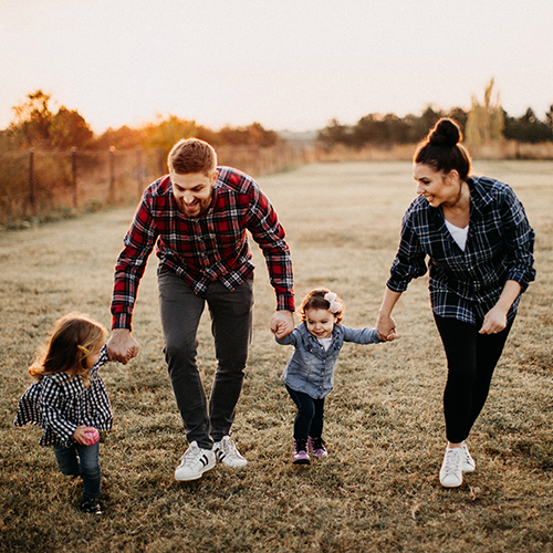 Smiling parents having fun holding hands with toddlers outside.