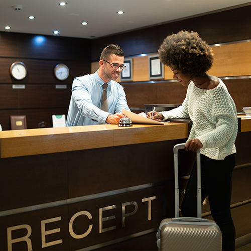 Woman checking into reception desk with suitcase.